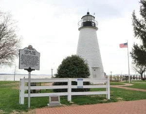 Historic Concord Point Lighthouse standing tall by the water with an American flag in Havre de Grace, Maryland. in Havre de Grace Scavenger Hunt, MD
