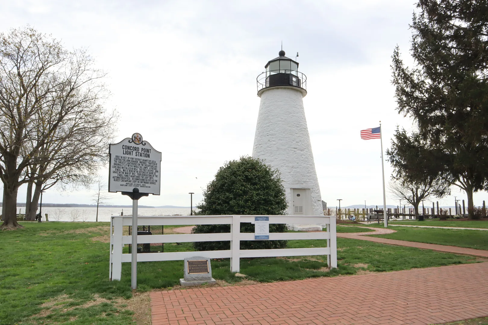Historic Concord Point Lighthouse standing tall by the water with an American flag in Havre de Grace, Maryland. in Havre de Grace Scavenger Hunt, MD