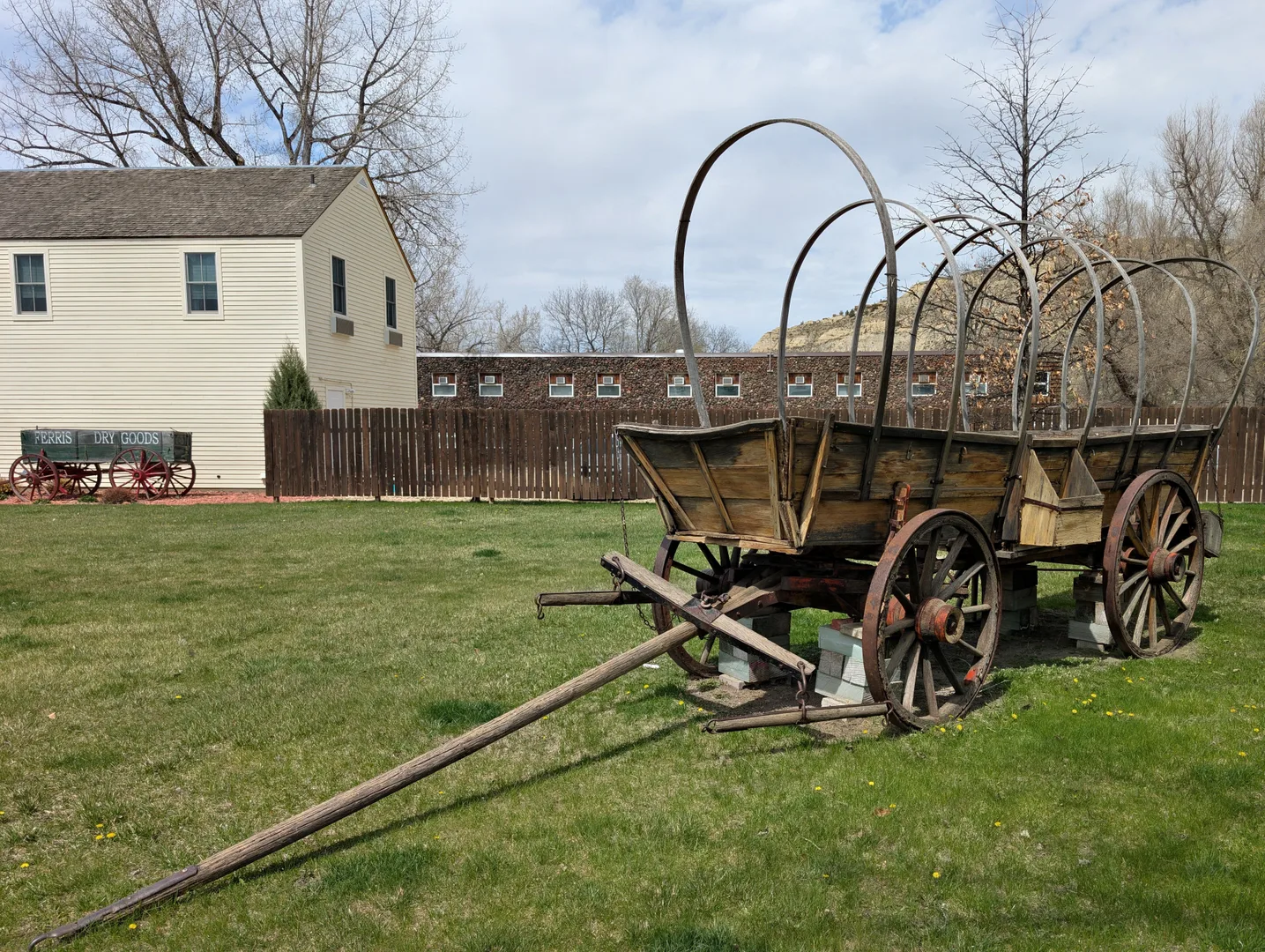A historical covered wagon displayed in a grassy area near a frontier-style building in Medora. in Medora Scavenger Hunt, ND